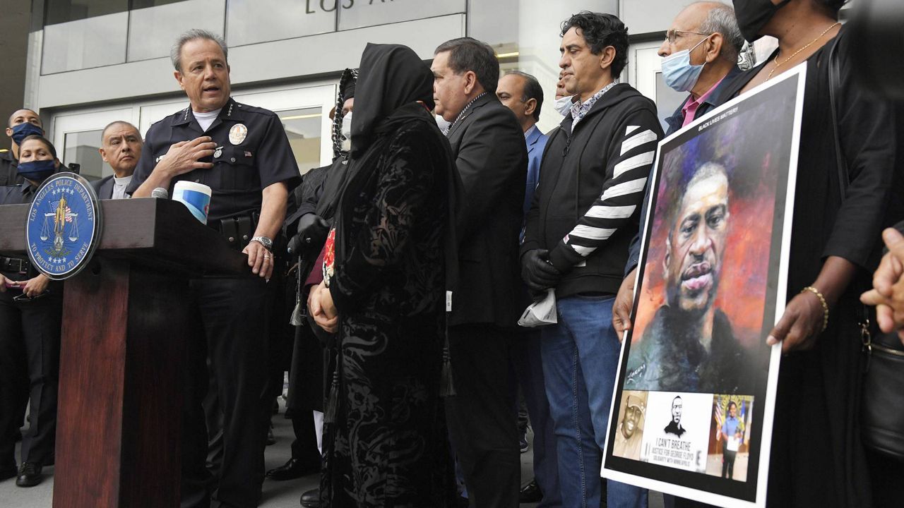 In this June 5, 2020 file photo, Los Angeles police chief Michel Moore, left, speaks as someone holds up a portrait of George Floyd during a vigil with members of professional associations and the interfaith community at LAPD headquarters. (AP/Mark J. Terrill)