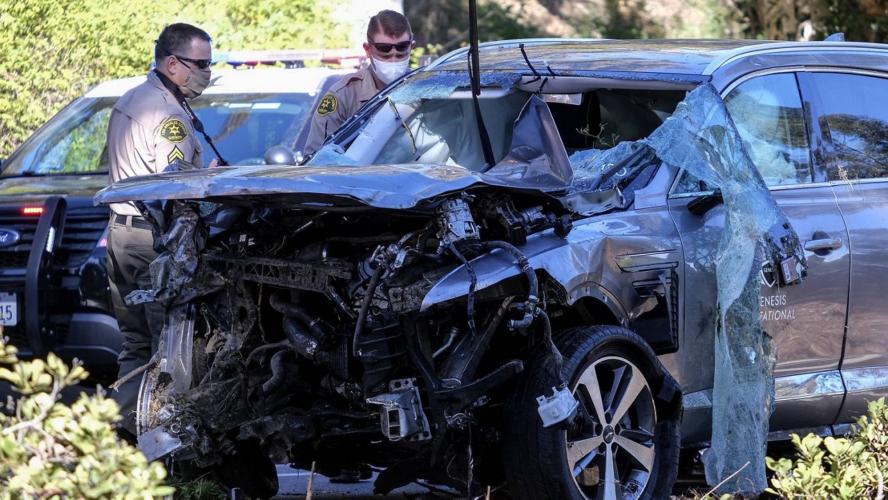 Law enforcement officers look over a damaged vehicle following a rollover accident involving golfer Tiger Woods, Tuesday, Feb. 23, 2021, in the Rancho Palos Verdes suburb of Los Angeles. Woods suffered leg injuries in the one-car accident and was undergoing surgery, authorities and his manager said. (AP Photo/Ringo H.W. Chiu)