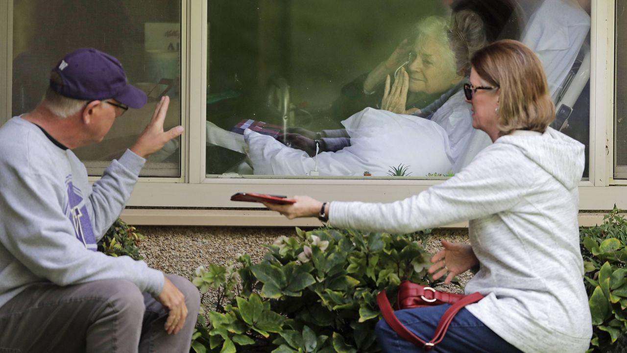 In this March 11, 2020, file photo, Judie Shape, who tested positive for the coronavirus, blows a kiss to family members through a window at the Life Care Center in Kirkland, Wash. (AP Photo/Ted S. Warren, File)