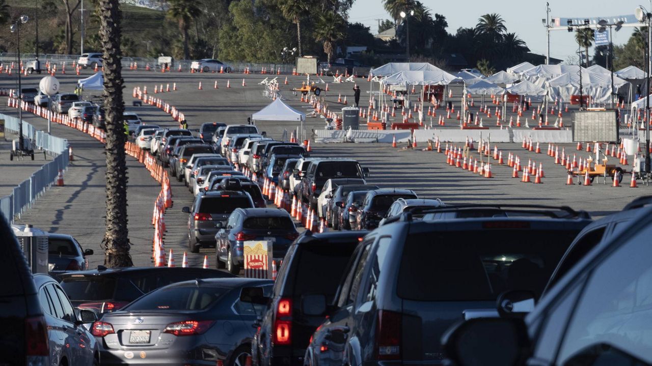 In this Jan. 26, 2021 file photo, Los Angeles residents wait in line in their cars to receive a covid-19 vaccine at Dodger Stadium. (AP Photo/Richard Vogel)
