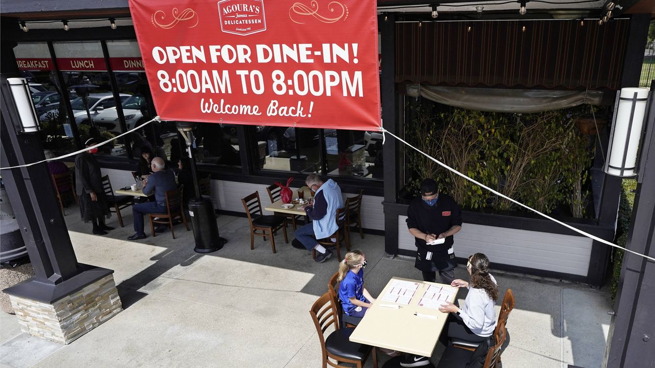 Diners Evie Costello, left, and Mandissa Costello, right, are served by Isaac Villaneva at Agoura's Famous Deli Sunday, March 14, 2021, in the Agoura Hills section of Los Angeles County. (AP Photo/Mark J. Terrill)