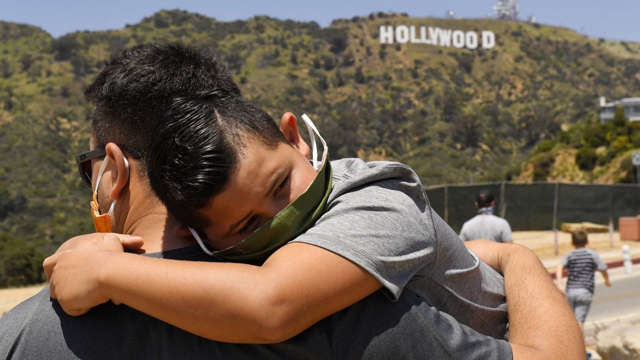 In this May 15, 2020, file photo, a father holds his son near the famed Hollywood sign during the coronavirus outbreak in Los Angeles. (AP Photo/Mark J. Terrill, File)