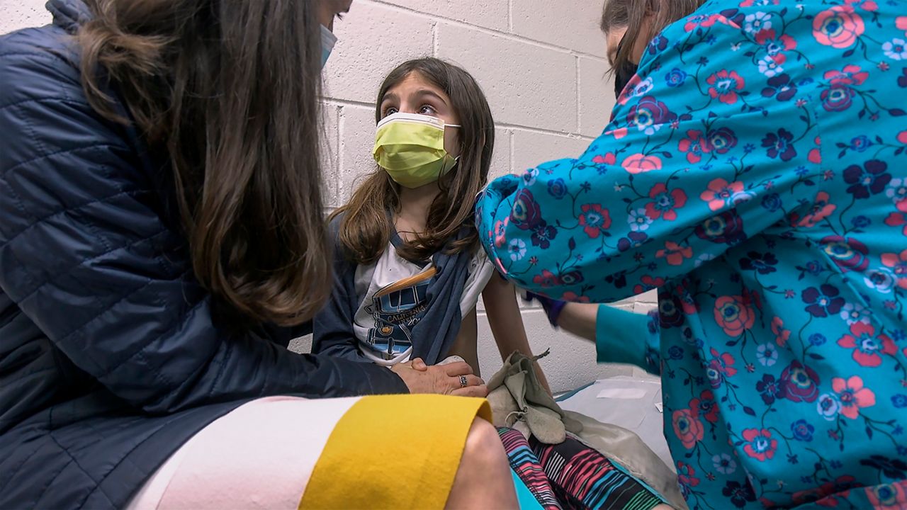 In this Wednesday, March 24, 2021 image from video provided by Duke Health, Alejandra Gerardo, 9, looks up to her mom, Dr. Susanna Naggie, as she gets the first of two Pfizer COVID-19 vaccinations during a clinical trial for children at Duke Health in Durham, N.C.