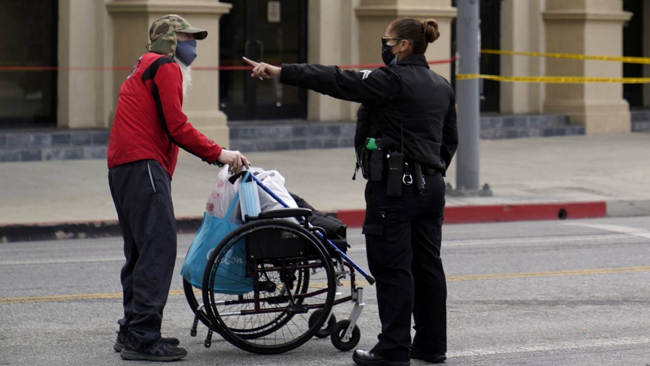 A senior with a wheelchair is diverted by a police officer, away from the closed perimeter of Echo Park Lake in Los Angeles, March 25, 2021. (AP Photo/Damian Dovarganes)