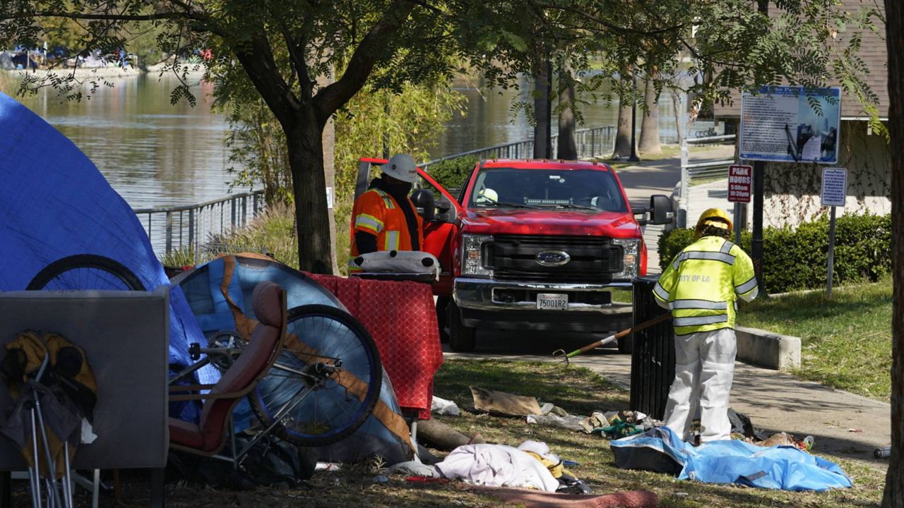 Los Angeles City LASAN CARE, Cleaning, and Rapid Engagement team members remove debris around tents on the south side of Echo Park Lake before their removal in LA, March 26, 2021. (AP Photo/Damian Dovarganes)