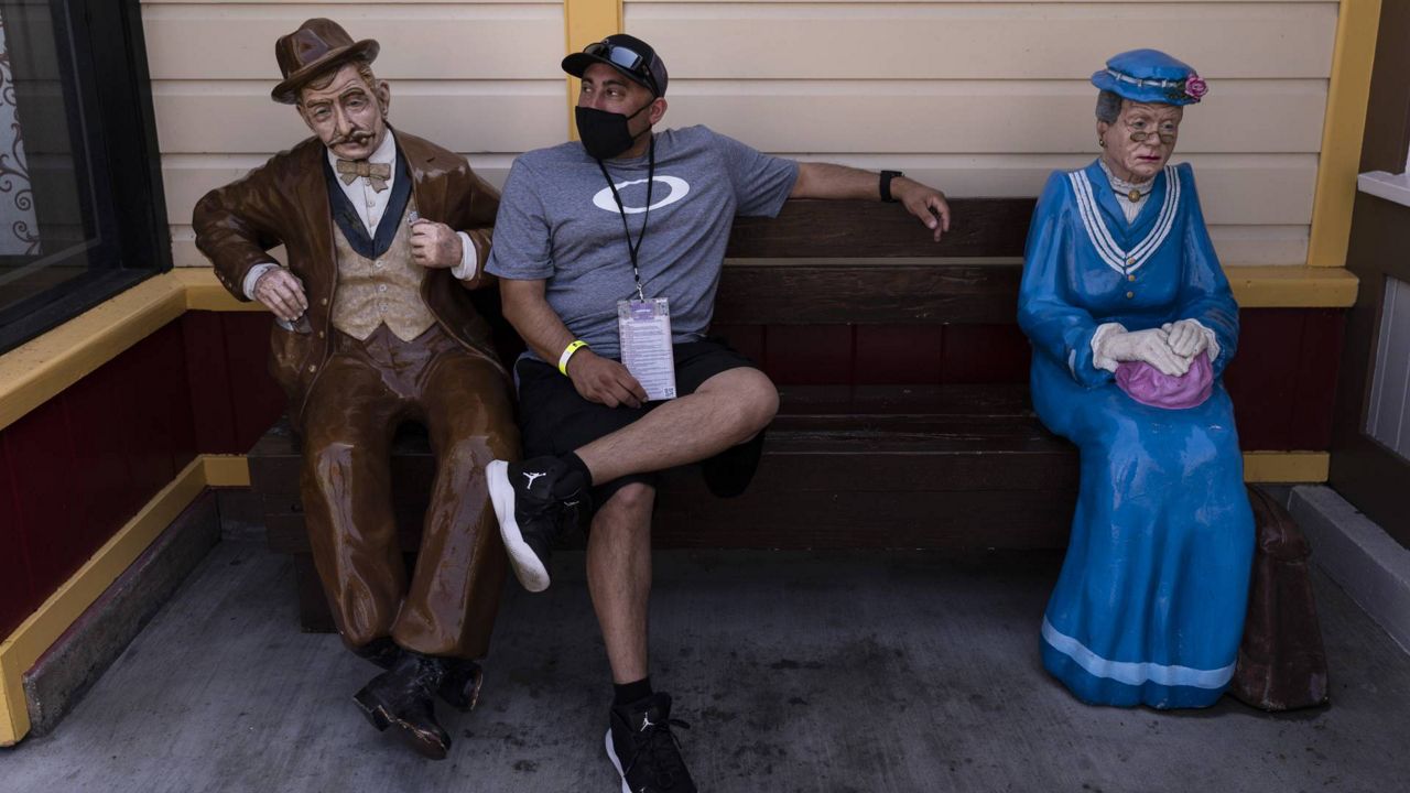 A visitor rests on a bench with two figures during the Knott's Taste of Boysenberry Festival at Knott's Berry Farm in Buena Park, Calif., Tuesday, March 30, 2021. (AP Photo/Jae C. Hong)