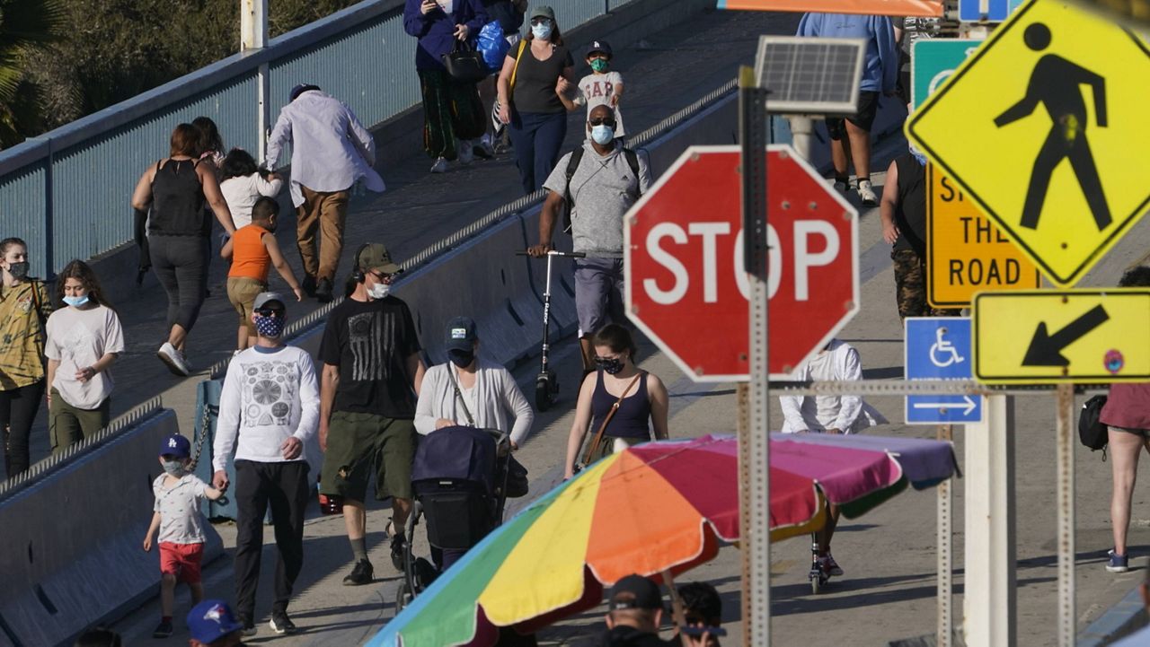 People walk down to the Santa Monica Pier Santa Monica, Calif., Wednesday, March 31, 2021. (AP Photo/Damian Dovarganes)