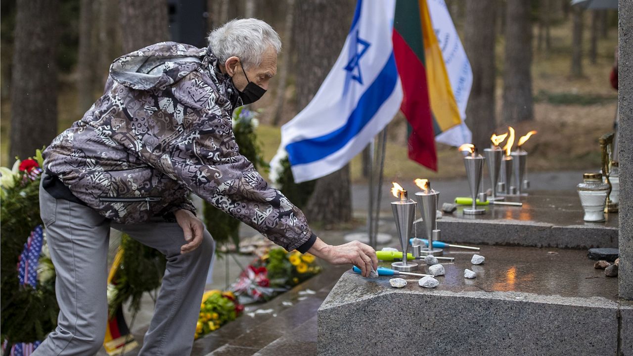 Holocaust survivor Davidas Leibzonas, wearing a face mask to protect against the coronavirus, places stones at the foot of a granite Holocaust survivor memorial in the Paneriai memorial during the ceremony marking the annual Holocaust Remembrance Day in Vilnius, Lithuania, Thursday, April 8, 2021. (AP Photo/Mindaugas Kulbis)