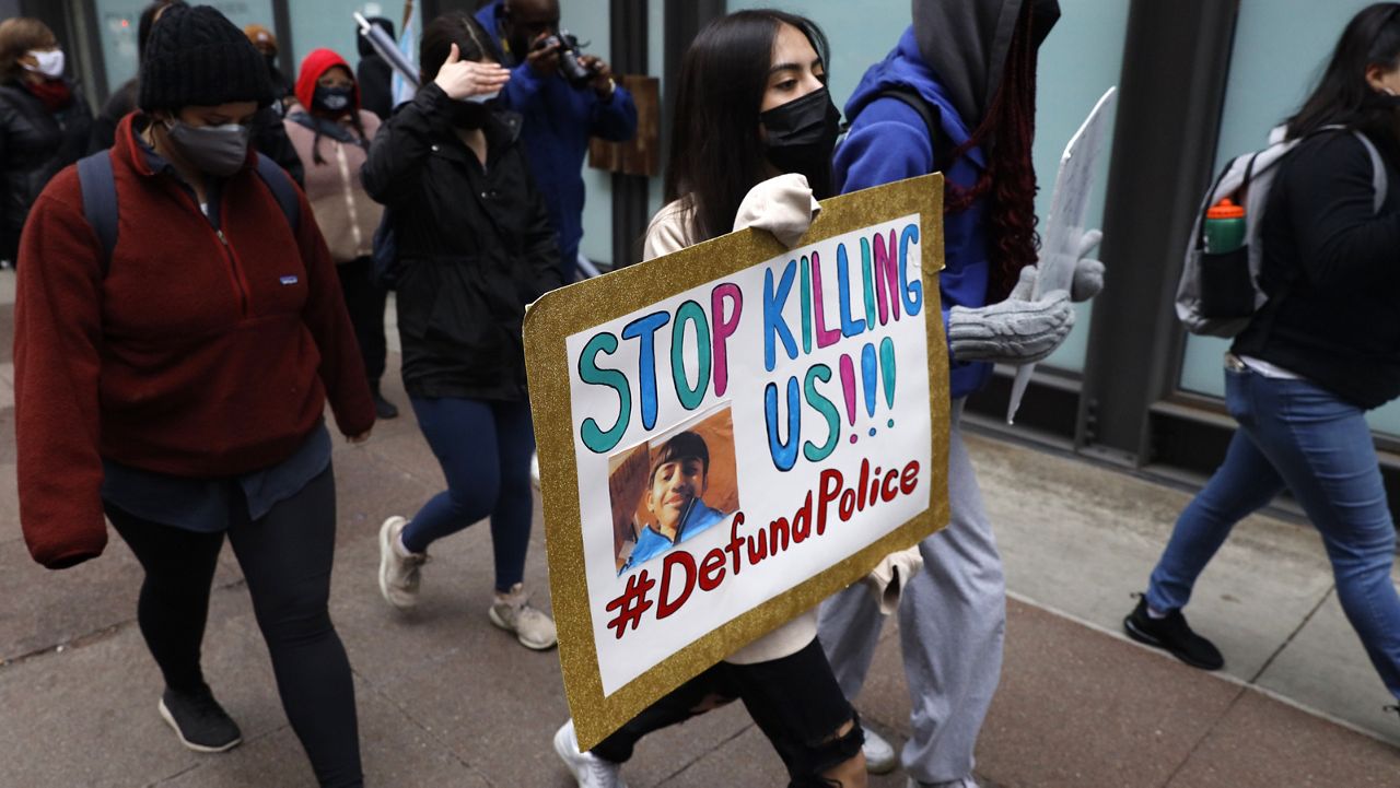 A protester holding a sign reading "Stop Killing Us" navigates along Chicago's Loop during a peaceful protest, Wednesday, April 14, 2021, ahead of the video release of the fatal police shooting of 13-year-old Adam Toledo. (AP Photo/Shafkat Anowar)