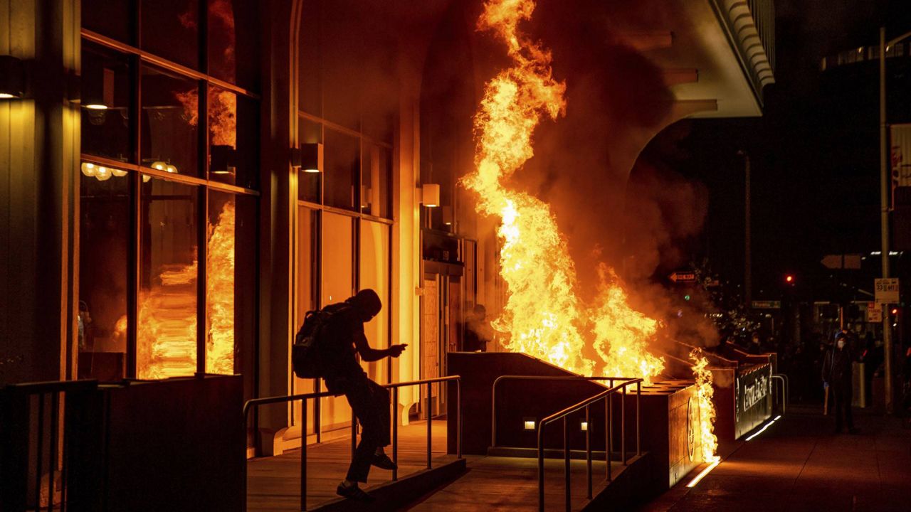 Demonstrators set fire to the front of the California Bank and Trust building during a protest against police brutality in Oakland, Calif., Friday, April 16, 2021. (AP Photo/Ethan Swope)