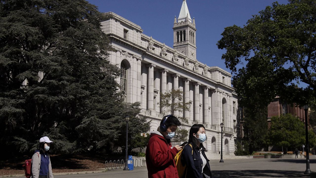 In this March 11, 2020, file photo, people wear masks while walking past Wheeler Hall on the University of California campus in Berkeley, Calif.