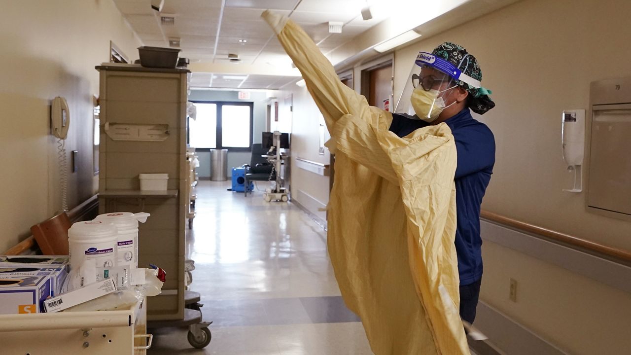 Registered Nurse Monica Quintana dons protective gear before entering a room at the William Beaumont hospital, April 21, 2021 in Royal Oak, Mich. Beaumont Health warned that its hospitals and staff had hit critical capacity levels. (AP Photo/Carlos Osorio)