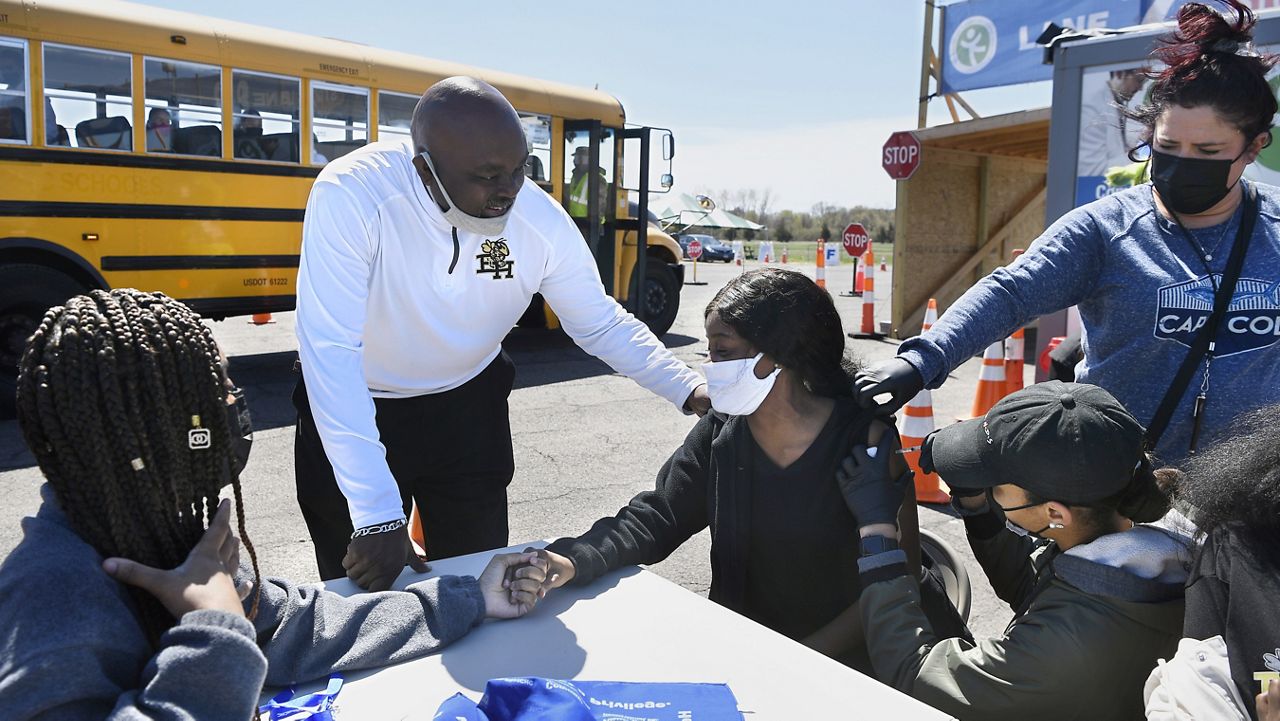 East Hartford High School senior Sudeen Pryce, right, center, receives support from classmate Alexia Phipps, left, East Hartford High School Intervention Coordinator Mark Brown, second from left, and EMT Katrinna Greene, top right, of Manchester, as RN Kaylee Cruz of Bristol administers a shot to Pryce at a mass vaccination site at Pratt & Whitney Runway in East Hartford, Conn., Monday, April 26, 2021. (AP Photo/Jessica Hill)