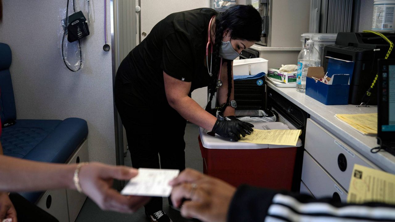 Nurse Natasha Garcia does paperwork after administering a dose of the Moderna COVID-19 vaccine to Magaly Esparza, foreground left, at a mobile clinic set up in the parking lot of a shopping center in Orange, Calif., April 29, 2021. (AP Photo/Jae C. Hong)
