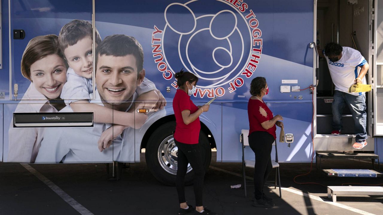 Two women wait in line to receive a dose of the Moderna COVID-19 vaccine at a mobile clinic set up in the parking lot of a shopping center in Orange, Calif., Thursday, April 29, 2021. (AP Photo/Jae C. Hong)