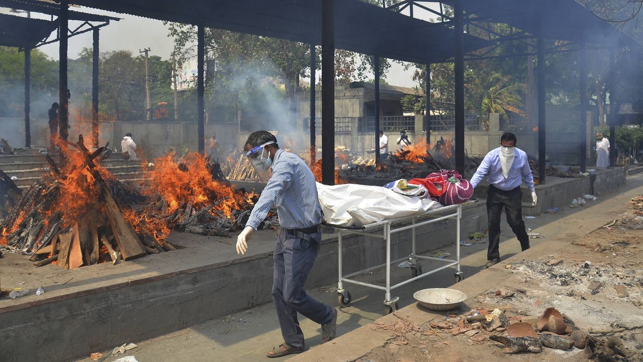 Relatives carry the body of a person who died of COVID-19 as multiple pyres of other COVID-19 victims burn at a crematorium Saturday in New Delhi.