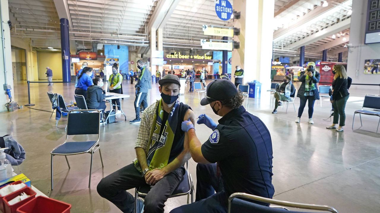 In this May 2, 2021 file photo, Austin Kennedy, left, gets the Johnson & Johnson COVID-19 vaccine at a clinic in a concourse at Lumen Field prior to an MLS soccer match between the Sounders and the LA Galaxy. (AP Photo/Ted S. Warren)