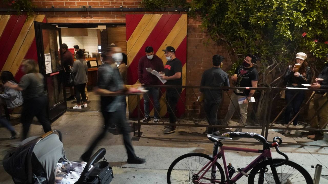 In this Sunday, May 2, 2021, photo, diners wait in line near the filled sidewalk tables of Wurstküche, eating sausages and drinking Belgian and German beer downtown LA. (AP Photo/Damian Dovarganes)