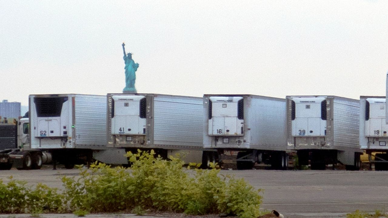 The Statue of Liberty is visible above refrigerator trucks intended for storing corpses that are staged in a lot at the 39th Street pier, in the Brooklyn borough of New York.