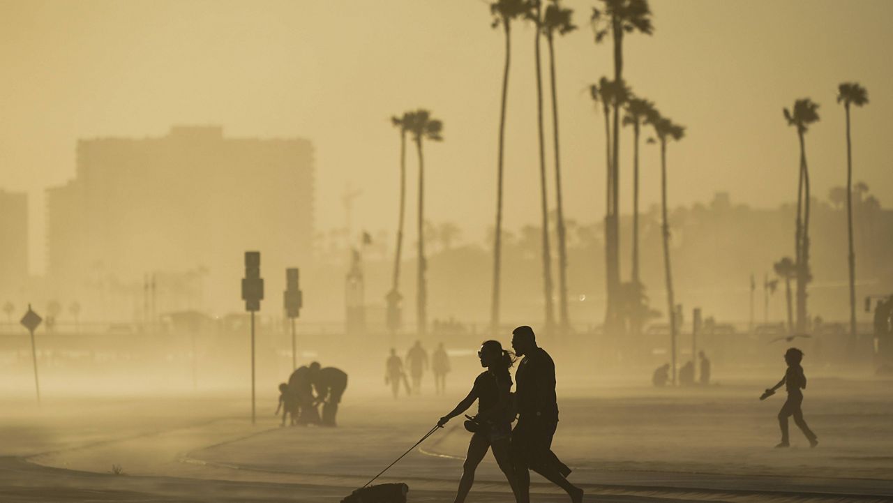 In this April 18, 2021, file photo, people walk on a beach path as evening winds kick up sand in Long Beach, Calif. (AP Photo/Ashley Landis, File)