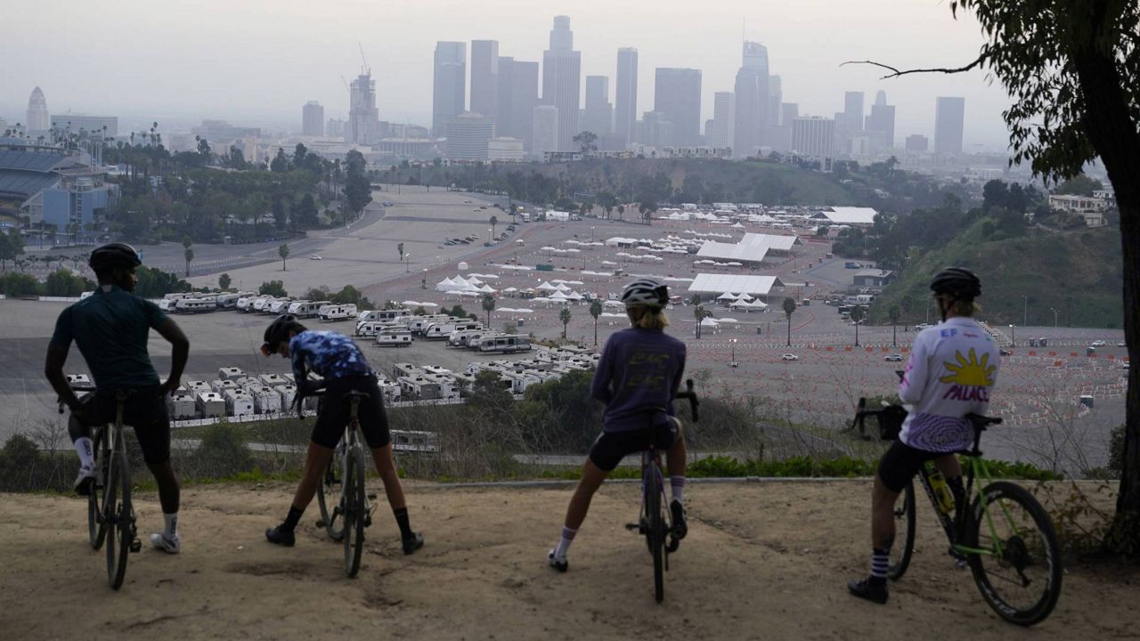 In this Feb. 11, 2021 file photo, cyclists rest atop a lookout point over a vaccination site at Dodger Stadium in Los Angeles. (AP Photo/Marcio Jose Sanchez, File)