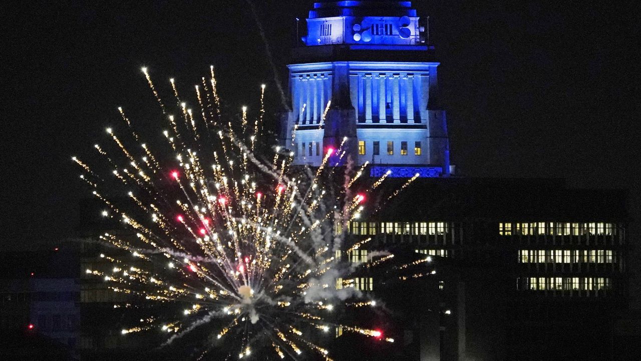 In this Oct. 27, 2020, file photo, Los Angeles City Hall is illuminated with dark blue lights as Dodgers fans celebrate with fireworks on Sunset Boulevard after watching the broadcast of Game 6 of the baseball World Series in Los Angeles. (AP Photo/Damian Dovarganes, File)