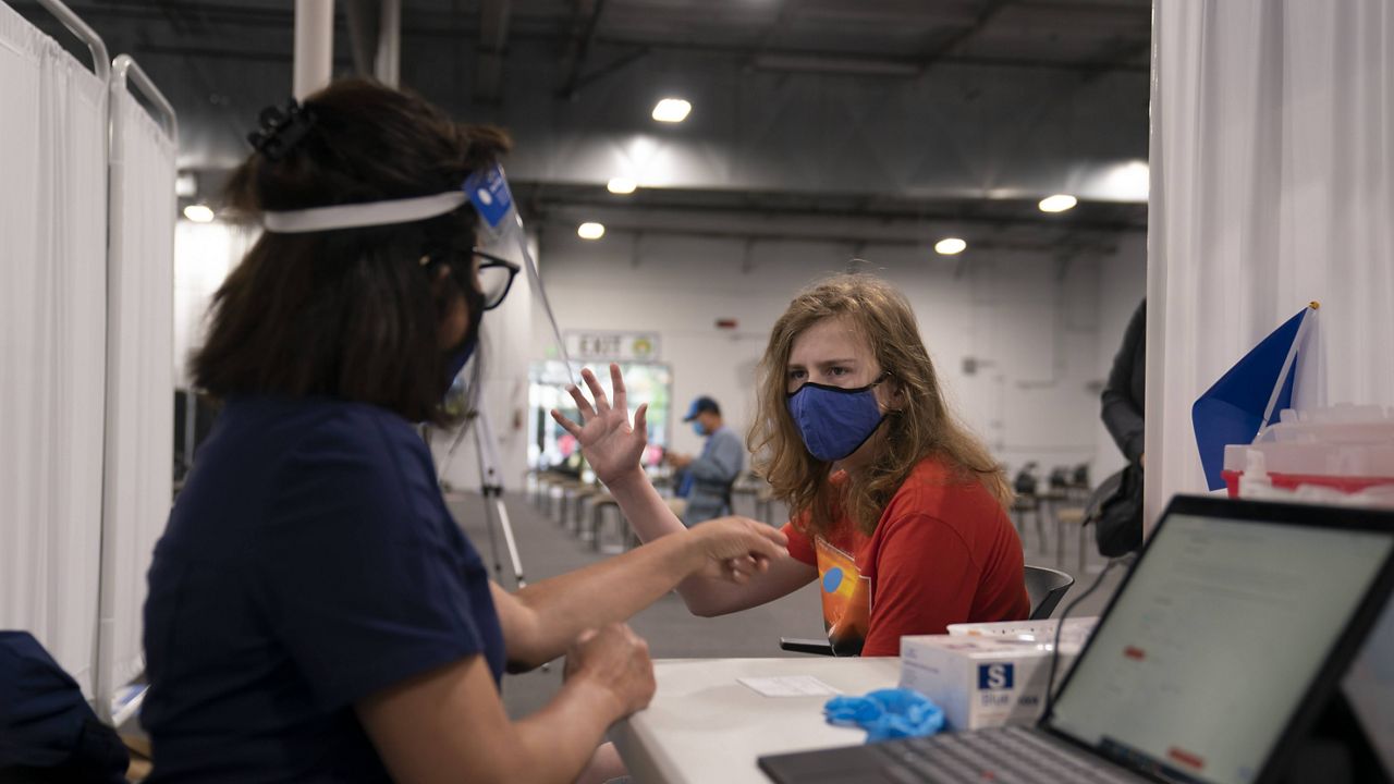 Garrette Parkison, 14, raises his writing hand as registered nurse Anna Ehrlich prepares to administer a dose of the Pfizer COVID-19 vaccine at Providence Edwards Lifesciences vaccination site in Santa Ana, Calif., Thursday, May 13, 2021. (AP Photo/Jae C. Hong)