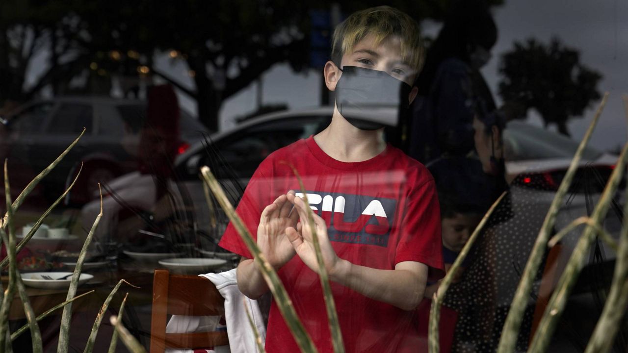 In this May 13, 2021 file photo, a child wears a mask while looking out the window of a beachfront restaurant in Santa Monica, Calif. (AP Photo/Marcio Jose Sanchez)