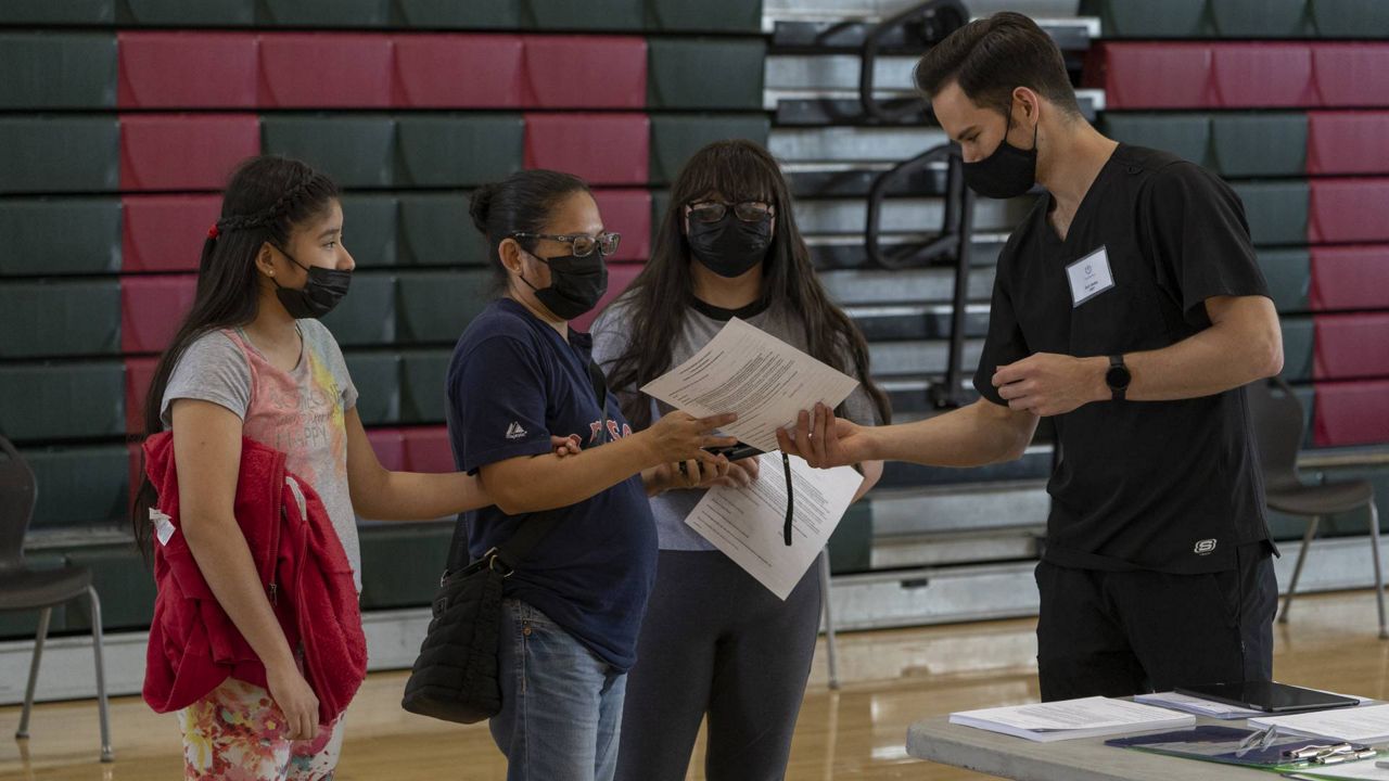 Emergency Medical Technician Seth Walley welcomes mother Guadalupe Cornejo, second from left, with daughters, Guadalupe Flores,15, right, and Estela Flores, 13, left, from East LA before they get vaccinated at the Esteban E. Torres High School in LA, May 27, 2021. (AP Photo/Damian Dovarganes)
