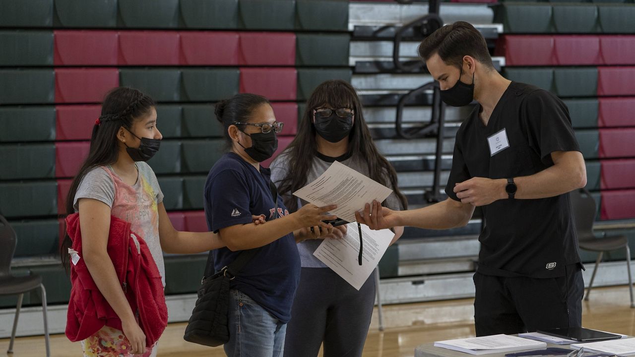 Emergency Medical Technician Seth Walley, right, welcomes mother Guadalupe Cornejo, second from left, with daughters, Guadalupe Flores,15, right, and Estela Flores, 13, left, from East Los Angeles before they get vaccinated with the Pfizer's COVID-19 vaccine at the Esteban E. Torres High School in Los Angeles Thursday, May 27, 2021. (AP Photo/Damian Dovarganes)