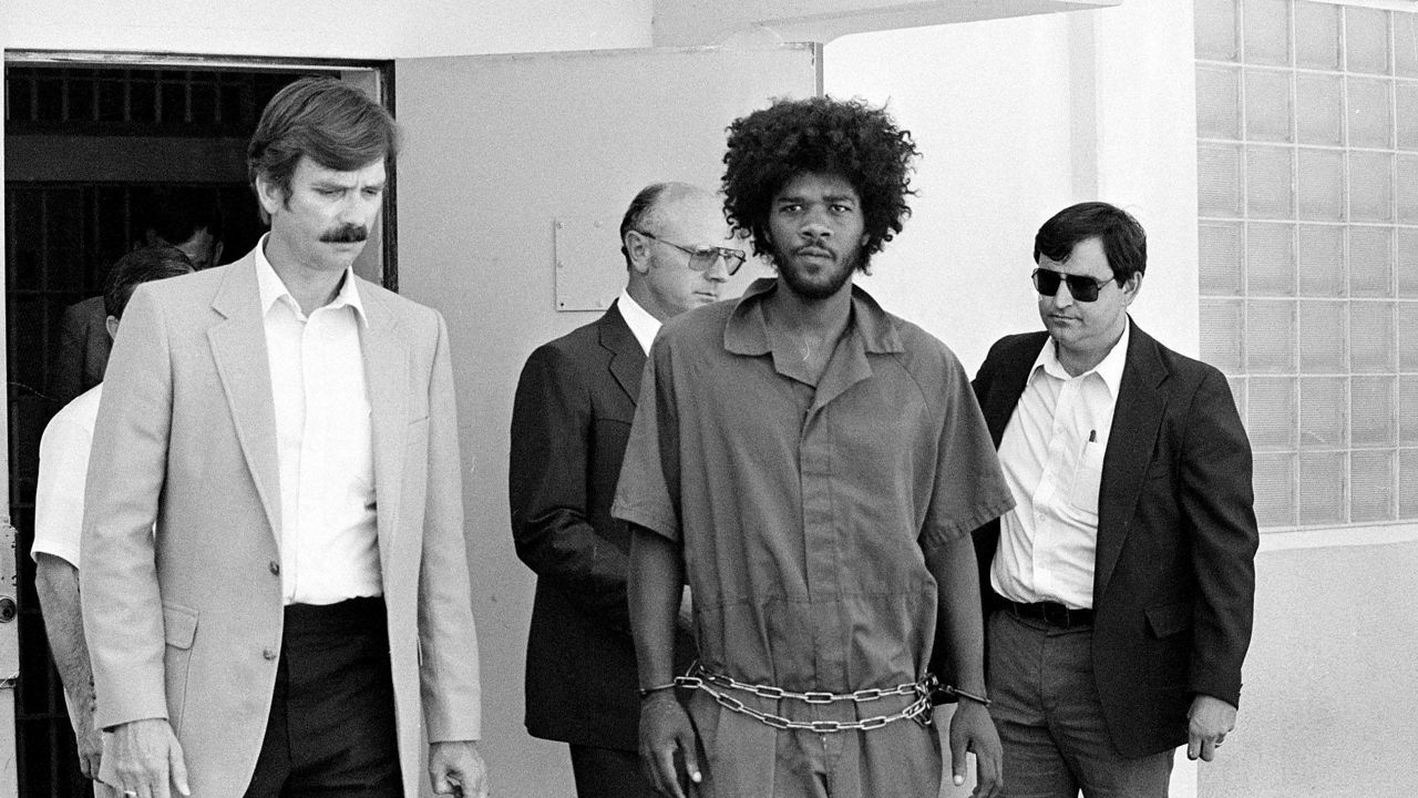 In this July 31, 1983, file photo, Kevin Cooper, center, a suspect in connection with the slashing death of four people in Chino, Calif., is escorted to a car for transport to San Bernadino from Santa Barbara, Calif., after he was arrested by police at Santa Cruz Island. (AP Photo/File)