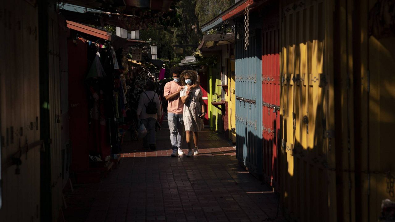 Alexia Thorpe and her boyfriend, Bennett Olupo are lit by afternoon sunlight as they stroll past stalls lining along Olvera Street in Los Angeles, June 4, 2021. (AP Photo/Jae C. Hong)