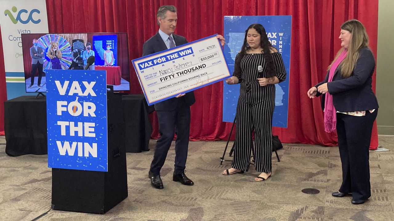 Gov. Gavin Newsom presents a check to Nancy Gutierrez, the winner of $50K lottery for getting vaccinated, as Assemblywoman Tasha Boerner Horvath, right, looks on in San Diego, Calif. on Friday, June 11, 2021. (AP Photo/Elliot Spagat)
