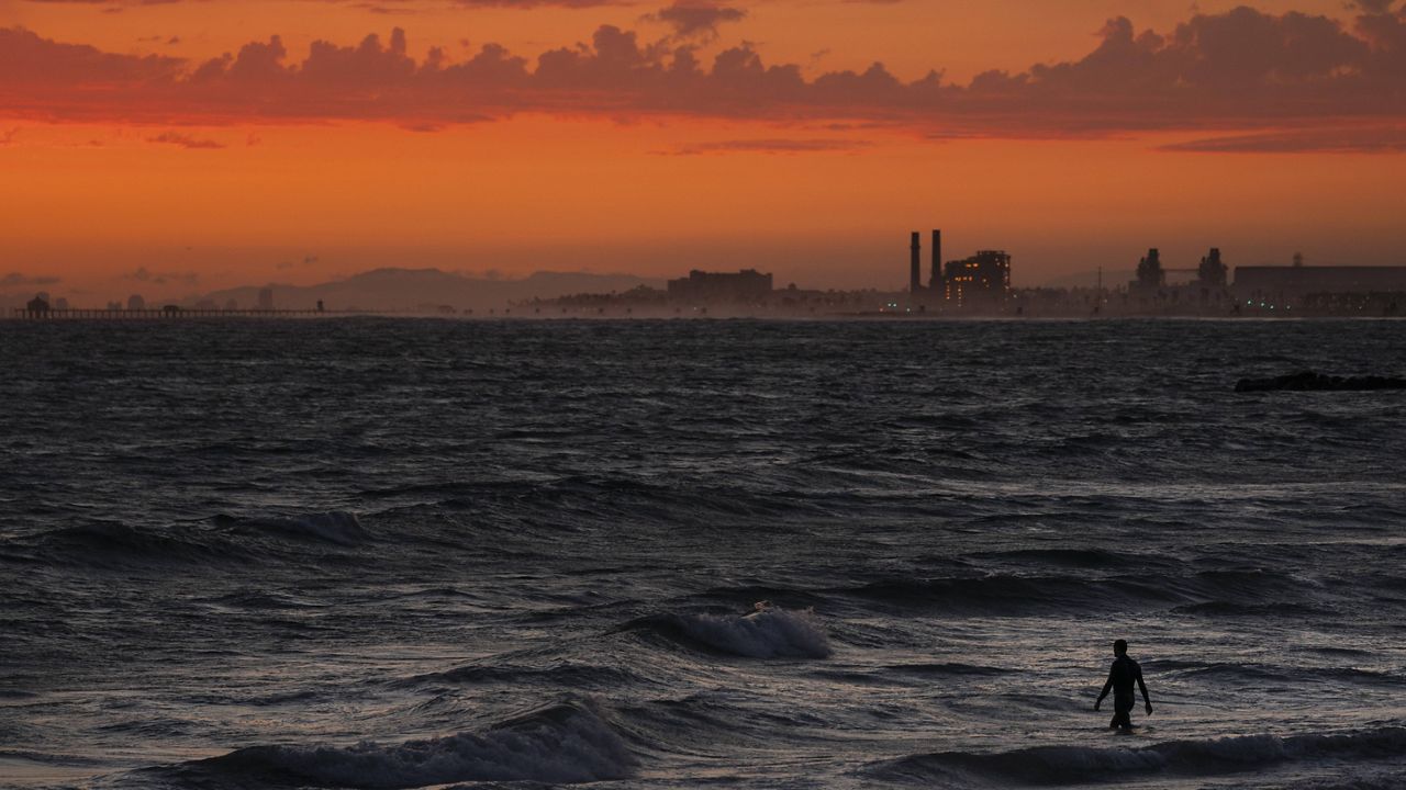 A man wades into the ocean at sunset, Tuesday, June 22, 2021, in Newport Beach, Calif. (AP Photo/Jae C. Hong)