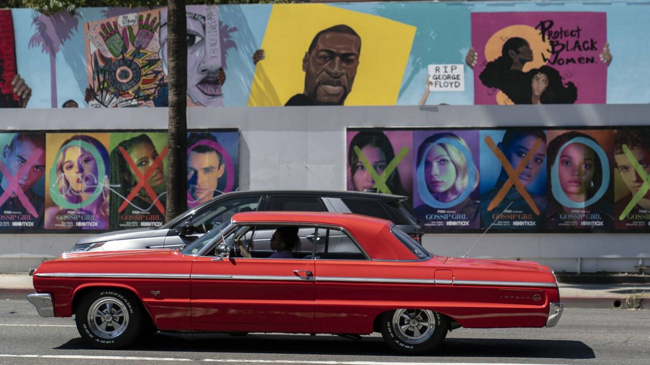 A vintage vehicle drives past the likeness of George Floyd seen on a Black Lives Matter artwork posted on Sunset Blvd. in Los Angeles, June 25, 2021. (AP Photo/Damian Dovarganes)