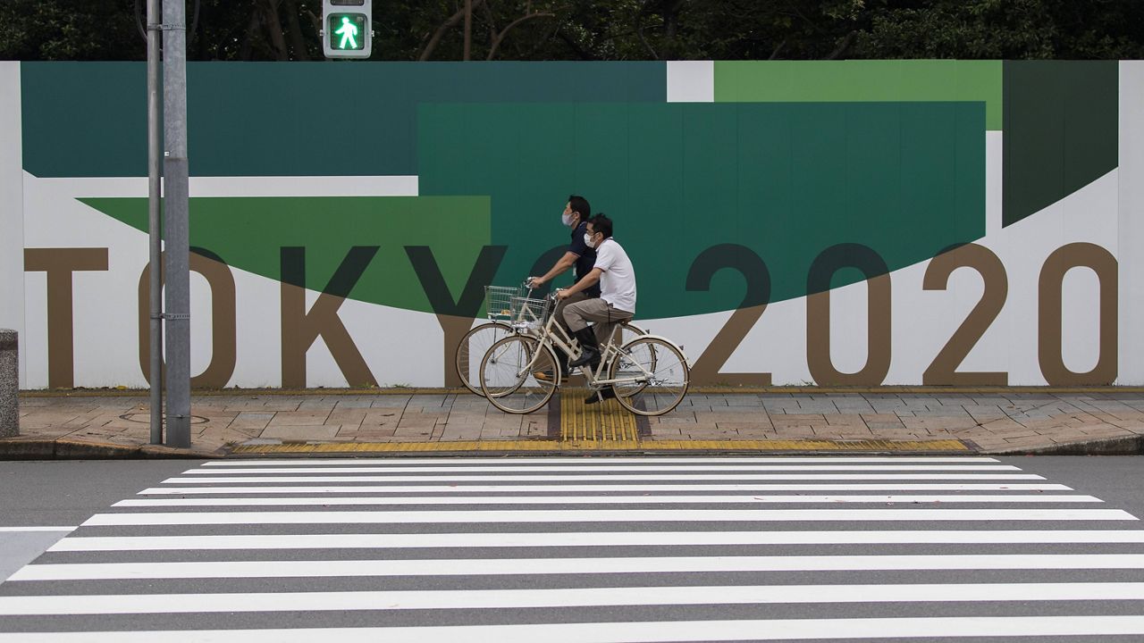 Men cycle Thursday along the wall installed to close off a park being prepared for the Olympics and Paralympics Games in Tokyo. (AP Photo/Hiro Komae, File)