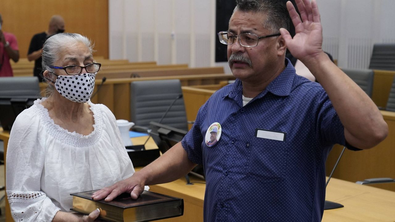 U.S. Marine Corps Hector Ocegueda holds his right hand on the Bible held by his mother, Amanda Dolores Rivera de Ocegeda, as he is administered with the citizenship oath by Judge Mark C. Scarsi in a federal courtroom in Los Angeles Friday, July 9, 2021. (AP Photo/Damian Dovarganes)