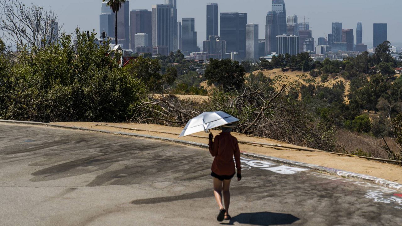 Athletes John Richardson, left, and wife, Sam use a pair of UV-Blocking Sun protection umbrellas while speed-walking in Elysian Park in Los Angeles Wednesday, July 7, 2021. (AP Photo/Damian Dovarganes)