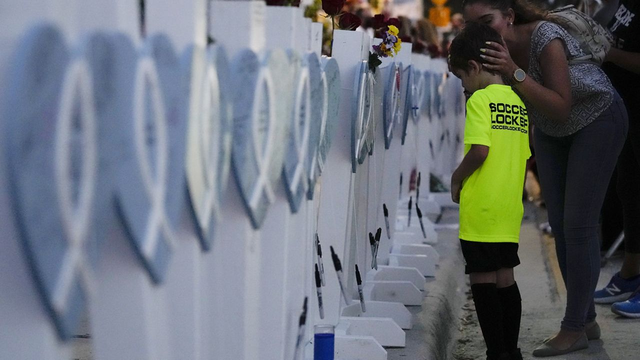 Claudia Benitez kisses the head of her son, David Barragan, 5, after he wrote a message on a wooden heart dedicated to Luis Bermudez, 26, one of the scores of victims of the Champlain Towers South condo building collapse, as people gathered for a multi-faith vigil near the site where the building once stood, Thursday, July 15, 2021, in Surfside, Fla. (AP Photo/Rebecca Blackwell)