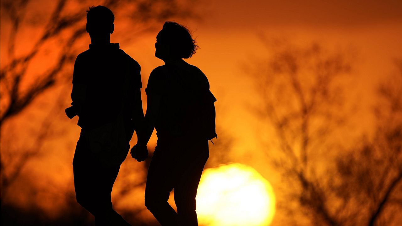 In this Wednesday, March 10, 2021, file photo, a couple walks through a park at sunset in Kansas City, Mo. (AP Photo/Charlie Riedel, File)