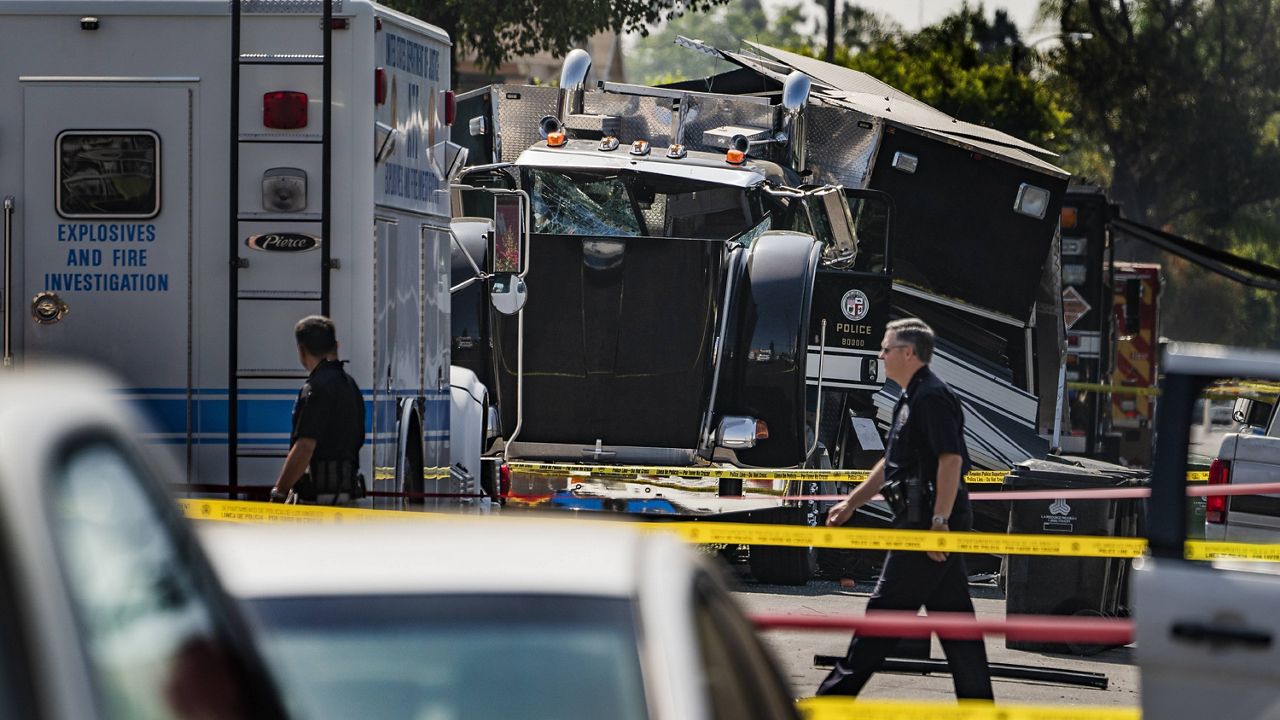 Police officers walk past the remains of an armored Los Angeles Police Department tractor-trailer on July 1, 2021, after illegal fireworks seized at a South Los Angeles home exploded, in South Los Angeles. (AP Photo/Damian Dovarganes)