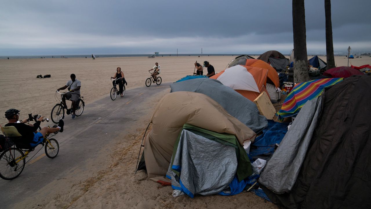 People ride their bikes past a homeless encampment set up along the boardwalk in the Venice neighborhood of Los Angeles, Tuesday, June 29, 2021. (AP Photo/Jae C. Hong)