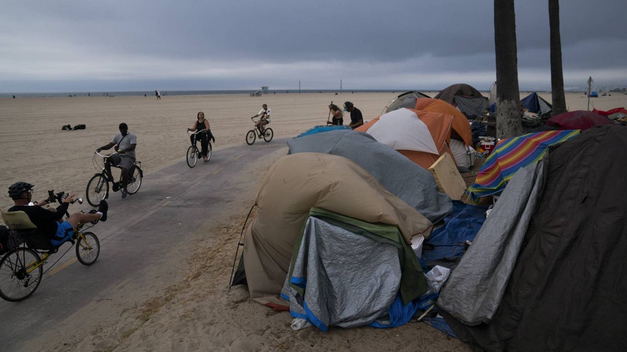People ride their bikes past a homeless encampment set up along the boardwalk in the Venice neighborhood of Los Angeles, June 29, 2021. (AP Photo/Jae C. Hong)