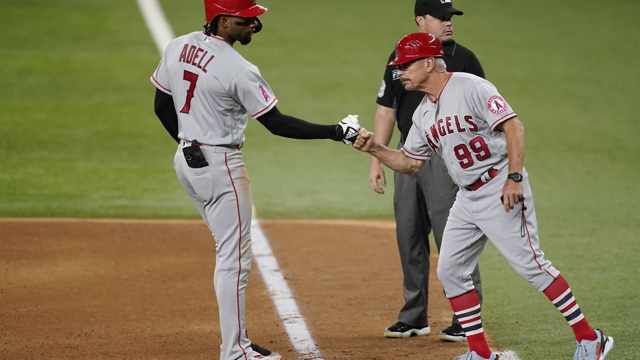 Los Angeles Angels' Jo Adell, left, celebrates his run-scoring single with first base coach Bruce Hines (99) in the seventh inning of a baseball game against the Texas Rangers as umpire Nick Mahrley stands by the bag in Arlington, Texas, Tuesday, Aug. 3, 2021. (AP Photo/Tony Gutierrez)