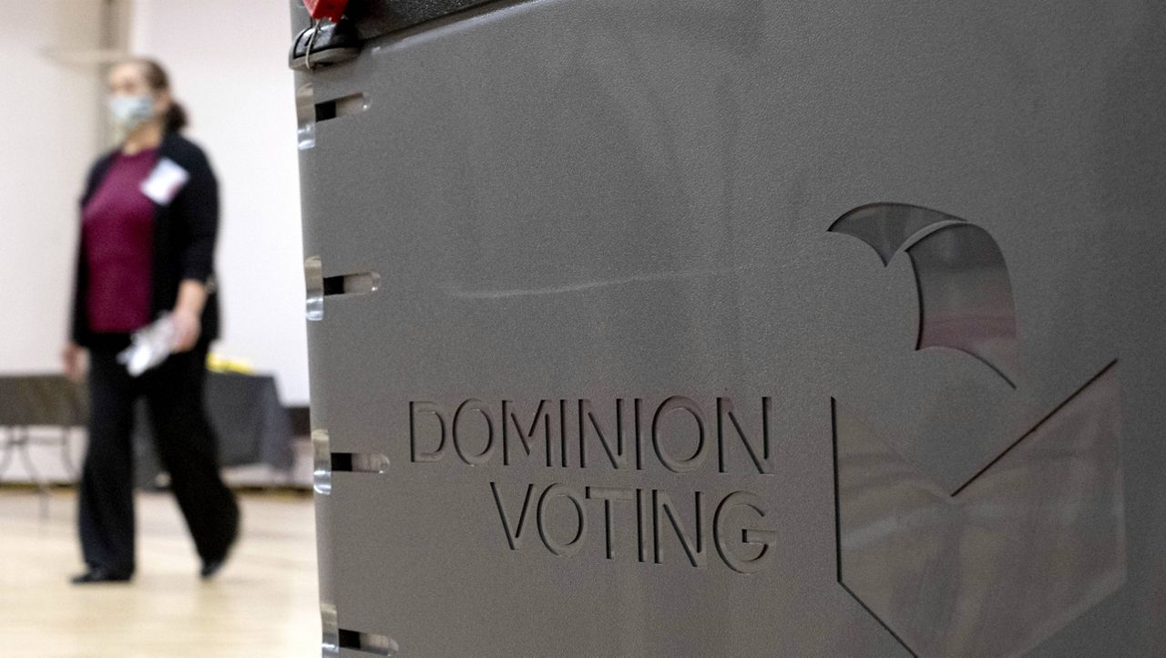 In this Jan. 4, 2021, file photo a worker passes a Dominion Voting ballot scanner while setting up a polling location at an elementary school in Gwinnett County, Ga. (AP Photo/Ben Gray, File)