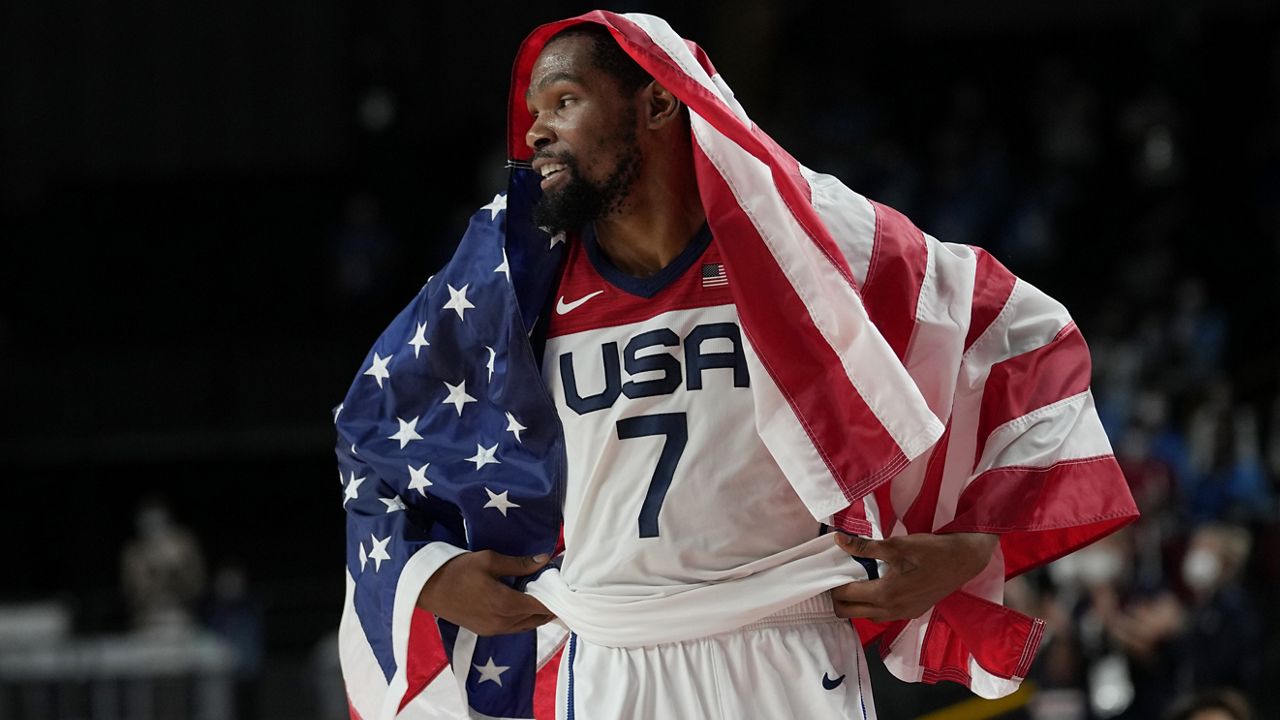 United States' Kevin Durant (7) drapes himself with a United States flag as he celebrates with teammates after their win over France in a men's basketball Gold medal game at the 2020 Summer Olympics, Saturday, Aug. 7, 2021, in Saitama, Japan. (AP Photo/Eric Gay)