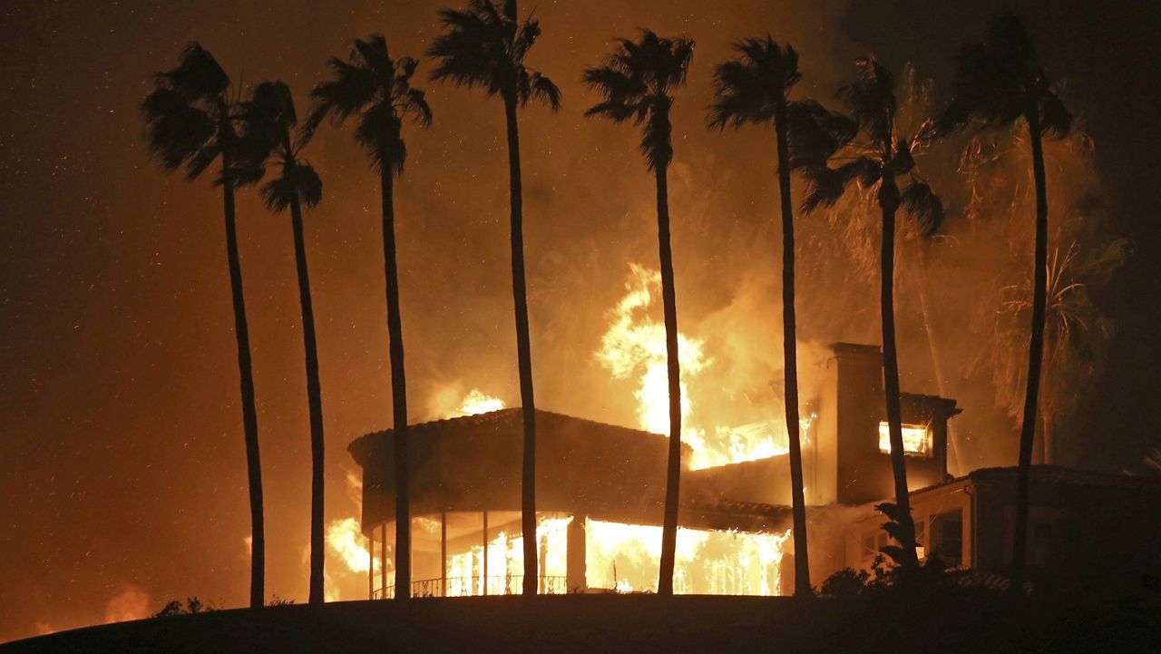 In this Nov. 9, 2018, file photo, palm trees frame a home being destroyed by the Woolsey wildfire above Pacific Coast Highway in Malibu, Calif. (AP Photo/Reed Saxon, File)