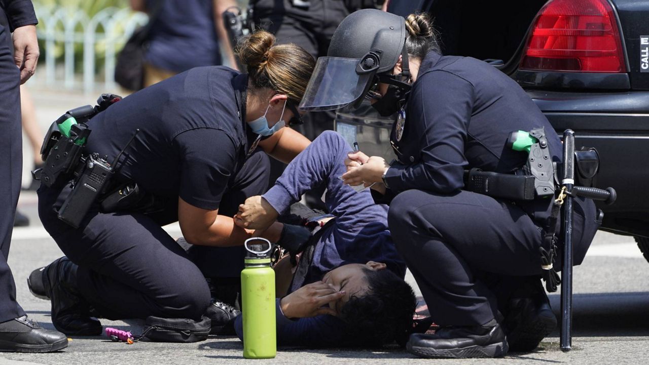 Los Angeles Police officer Gutierrez, left, puts pressure on the open wound of a demonstrator, who was stabbed during clashes between anti-vaccination demonstrators and counter-protesters in front of the City Hall in LA on Saturday, Aug. 14, 2021. (AP Photo/Damian Dovarganes)