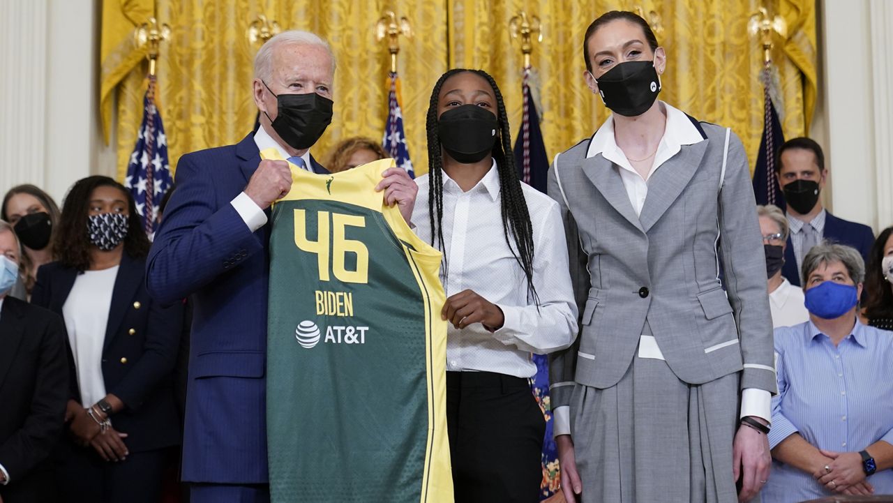 President Joe Biden, left, poses for a photo with Seattle Storm's Jewell Loyd, center, and Breanna Stewart, right, during an event in the East Room of the White House in Washington, Monday, Aug. 23, 2021, to celebrate their 2020 WNBC Championship. (AP Photo/Susan Walsh)