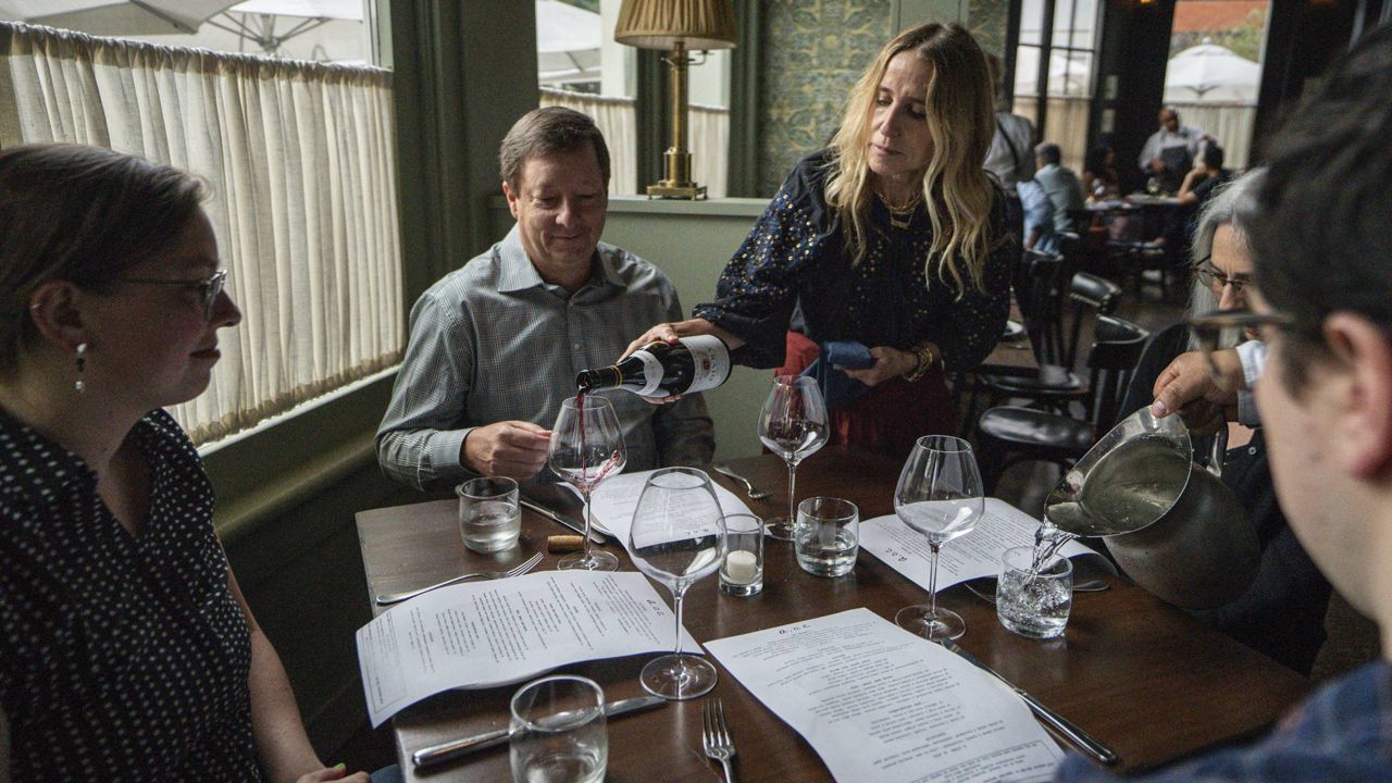 In this June 19, 2021, file photo, Caroline Styne, owner and wine director at The Lucques Group, serves wine to attorney Alec Nedelman at the A.O.C. Brentwood restaurant in Los Angeles. (AP Photo/Damian Dovarganes)